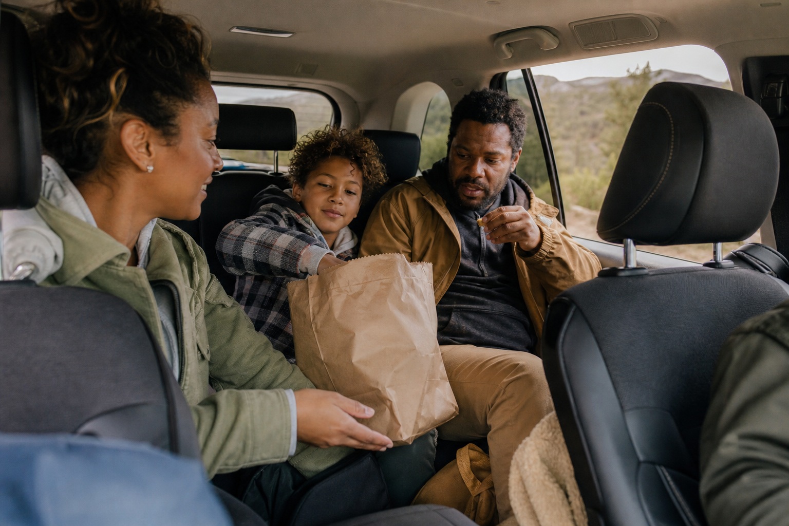 Candid travelers sitting inside a car during a road trip with a snack bag.