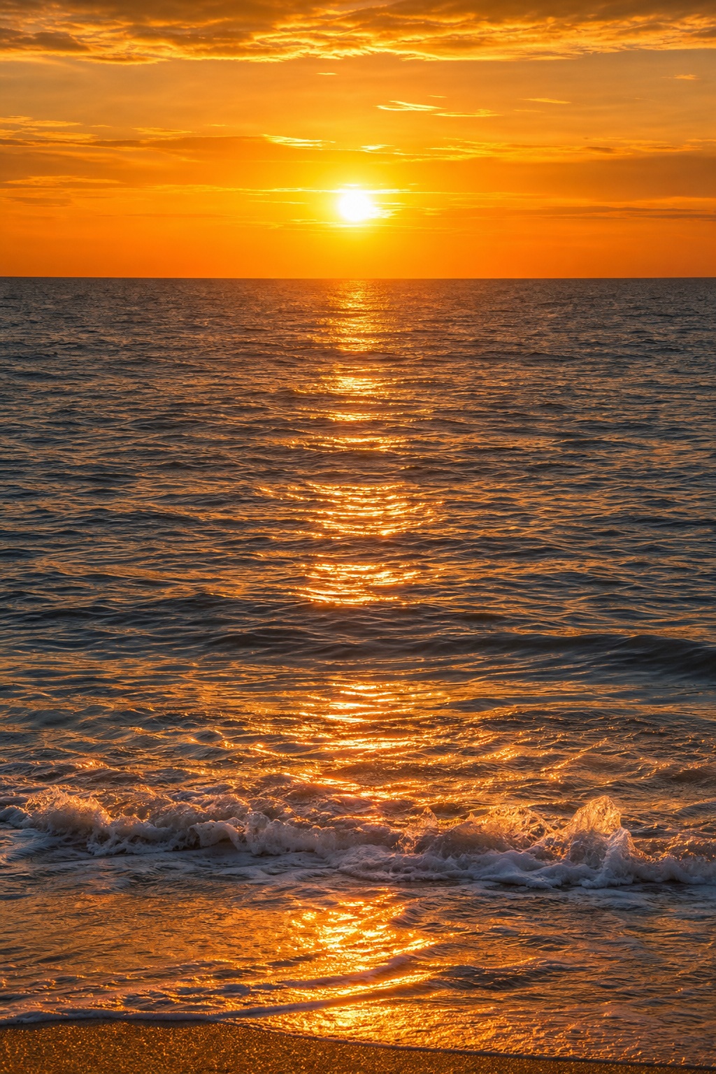 Golden sunset reflecting on ocean waves above a sandy beach shoreline.