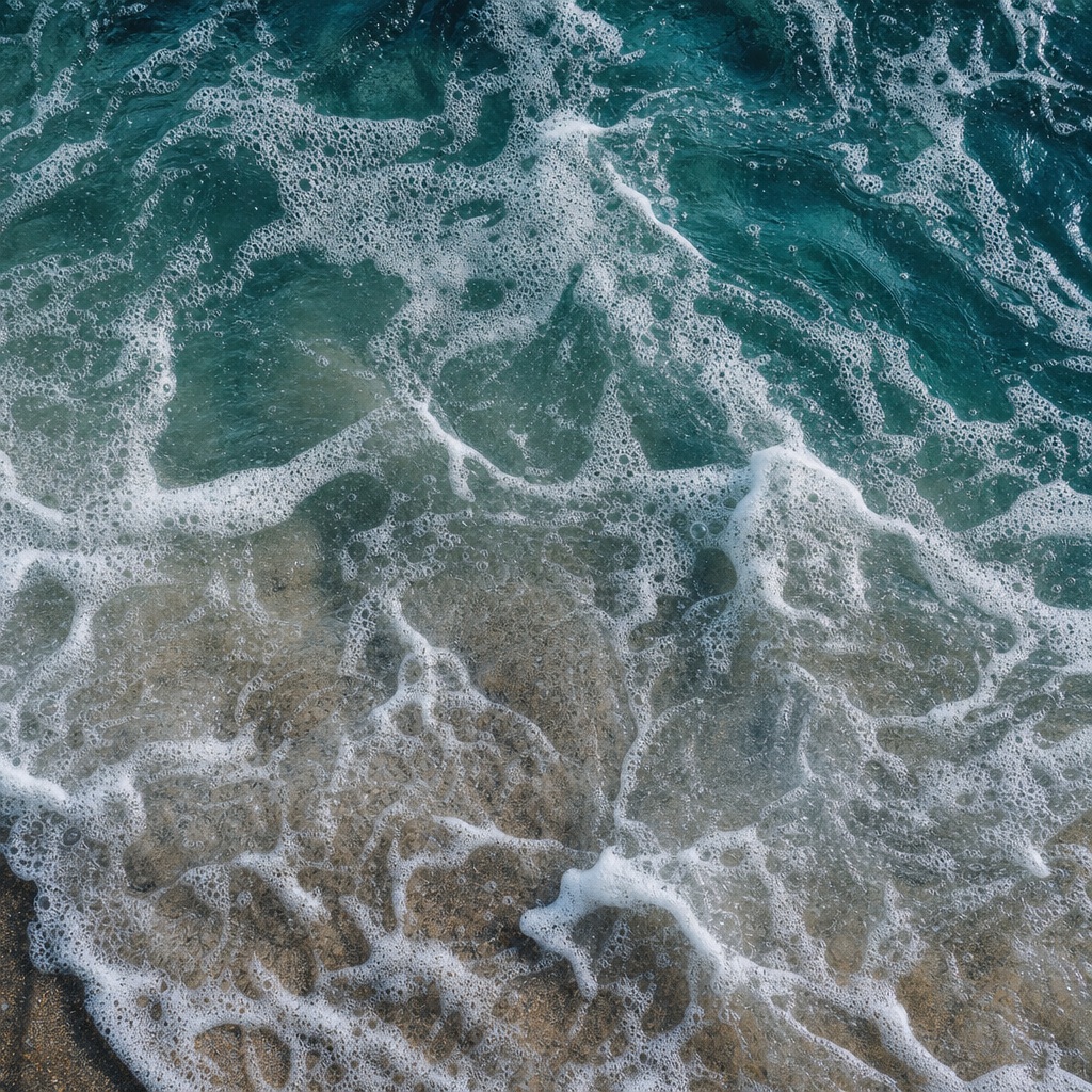 Deep teal ocean water with white sea foam washing over wet sand