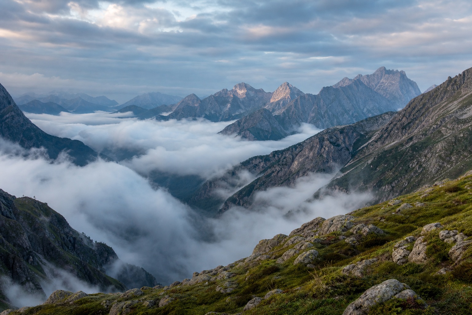 Misty mountain peaks rising above a cloud-filled valley and rocky foreground.