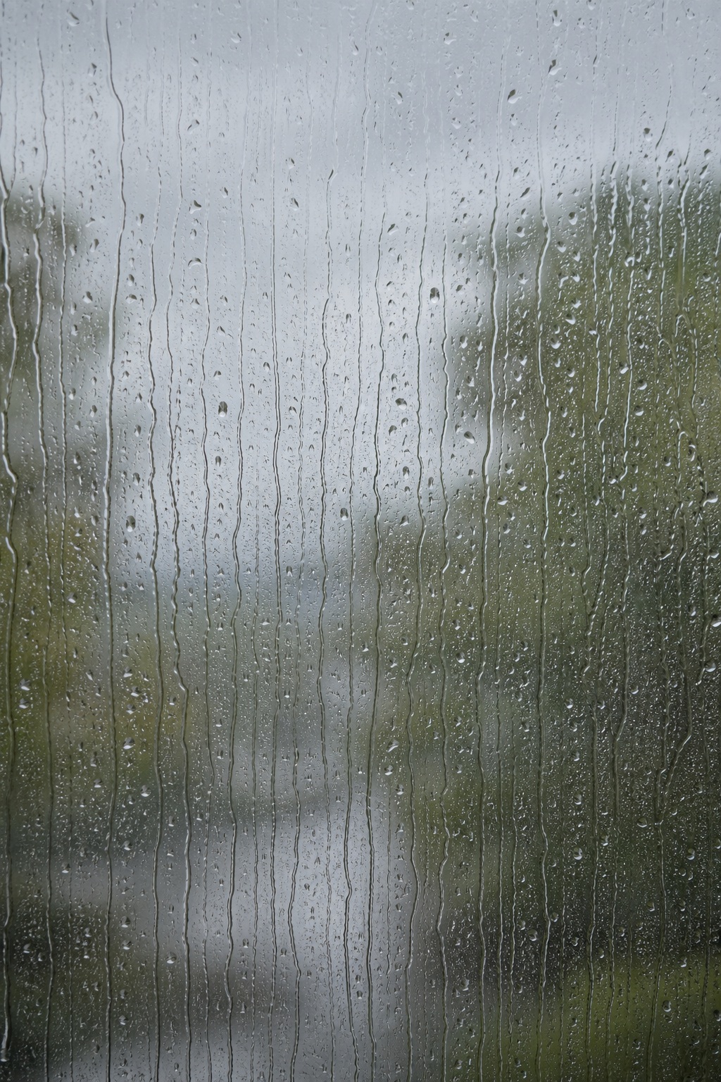 Rain streaks running down a window with soft blurred background lights