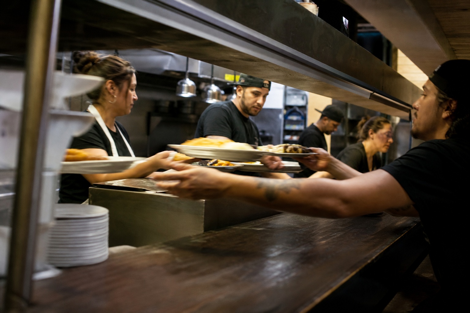 People reaching across a diner counter as plates are passed in a late night scene.