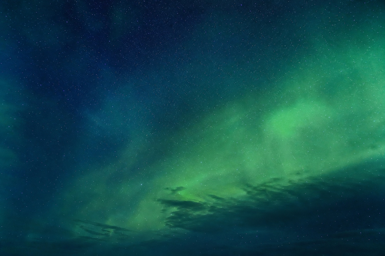 Green aurora lights sweeping across a dark night sky with faint stars and clouds.