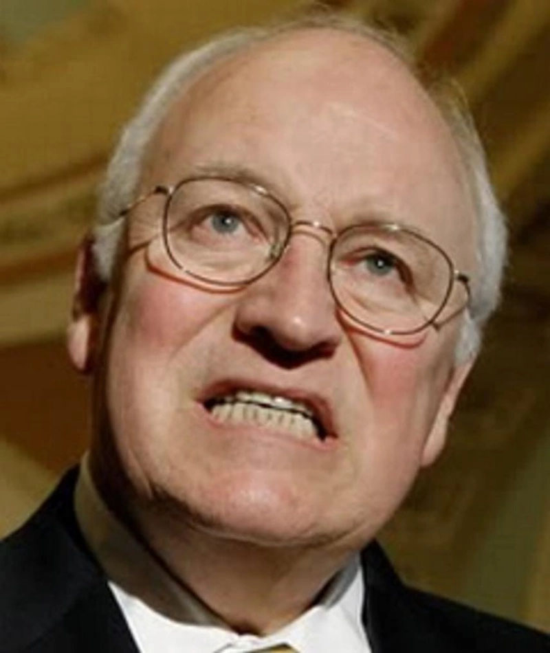 Close-up portrait of a mature businessman wearing glasses and a suit, grimacing slightly.