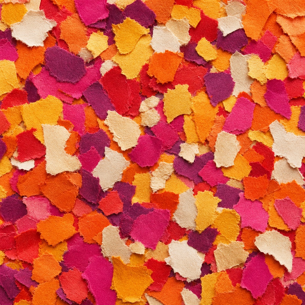 Colorful torn paper confetti pieces in orange, pink, cream, and red.