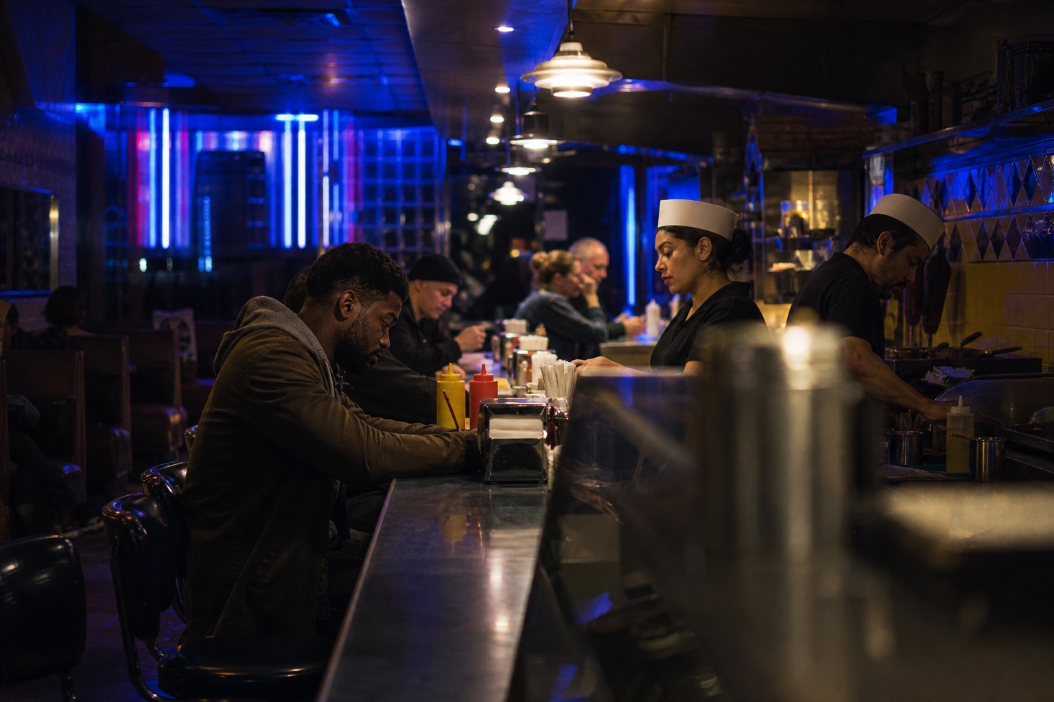 People sitting at a dimly lit diner counter late at night.