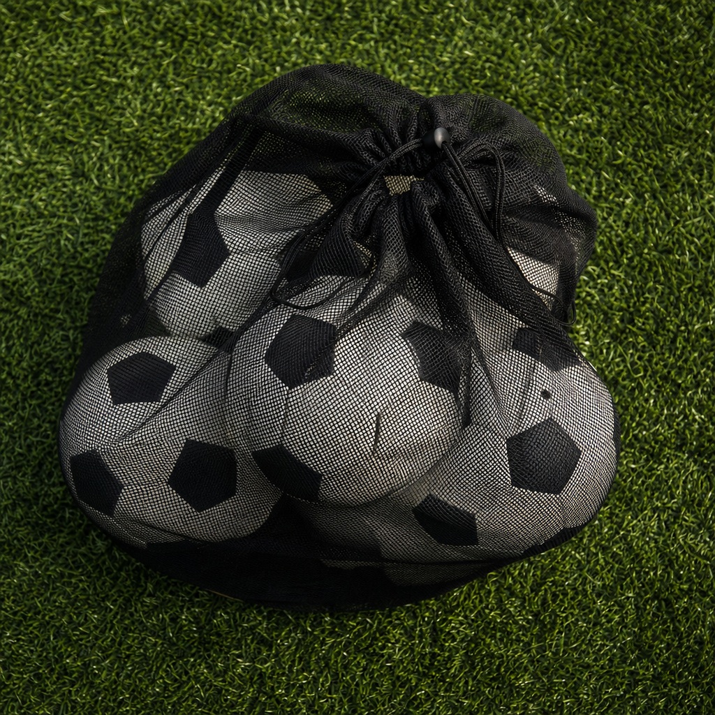 A mesh bag filled with soccer balls sitting on green turf.