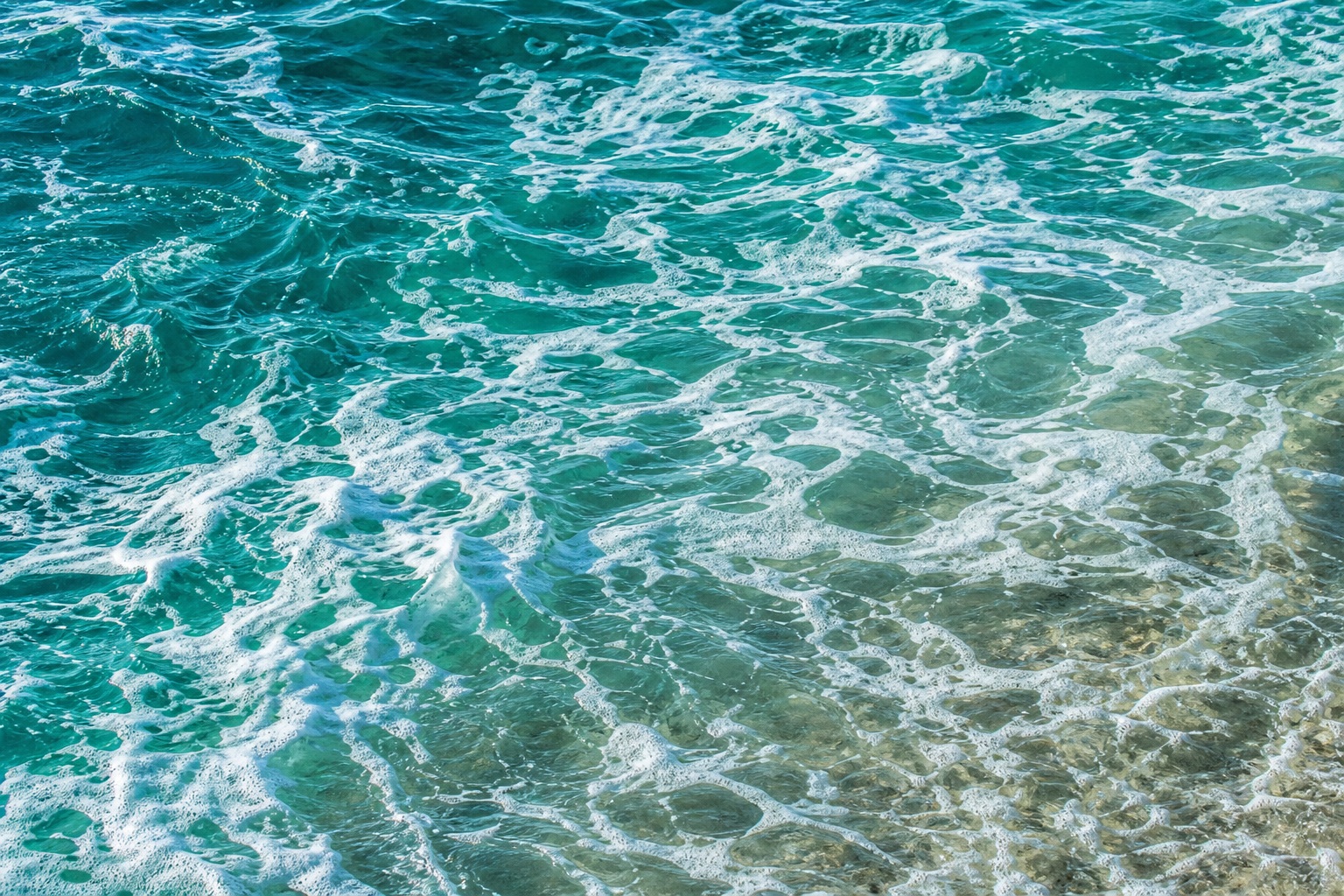 Blue ocean water with white sea foam and rippling shoreline texture
