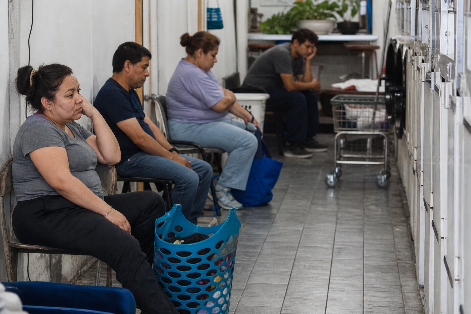 People seated and waiting in a laundromat beside a row of washing machines.