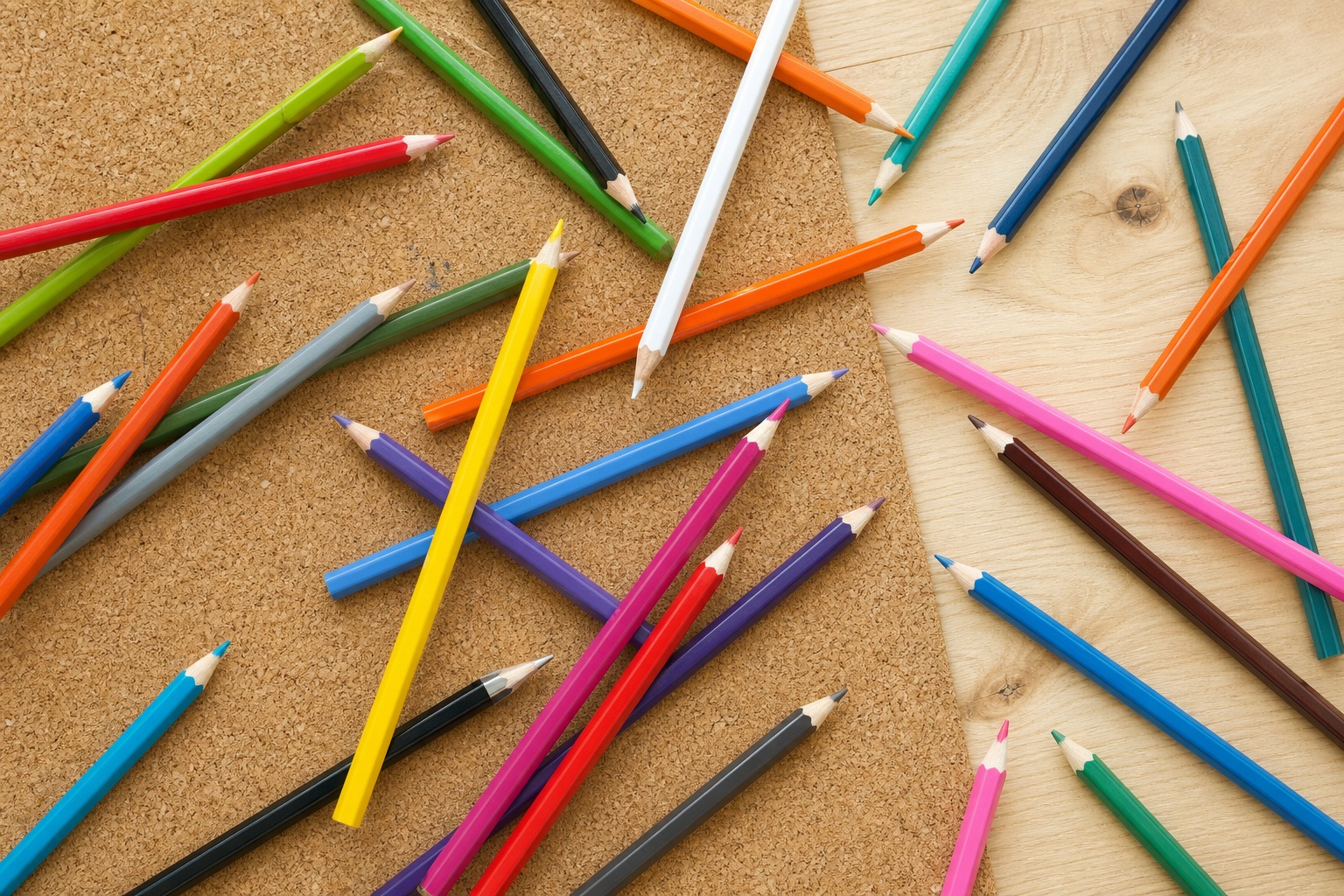 Colored pencils scattered on a cork mat in a clean flat lay view.