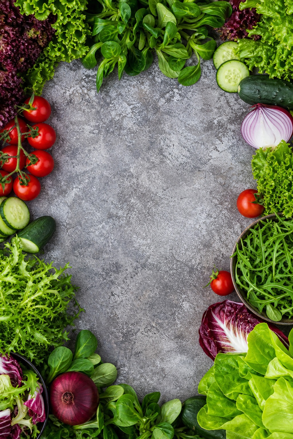Fresh salad ingredients arranged around a gray stone center on a vertical flat lay.