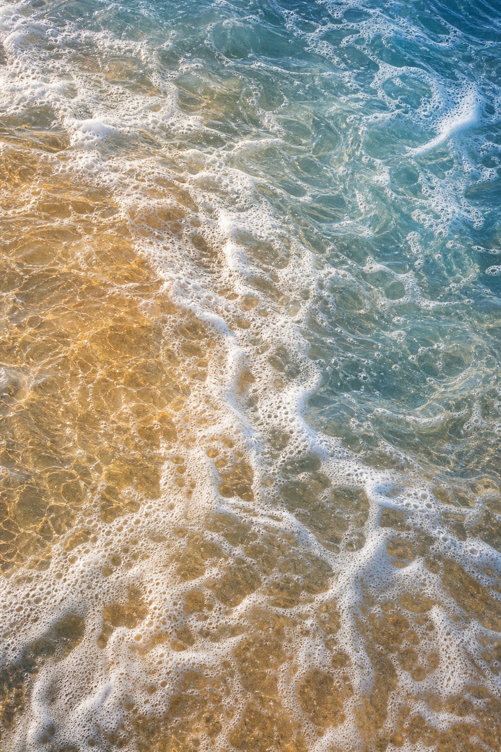 Golden sunlight over swirling white sea foam and blue coastal water