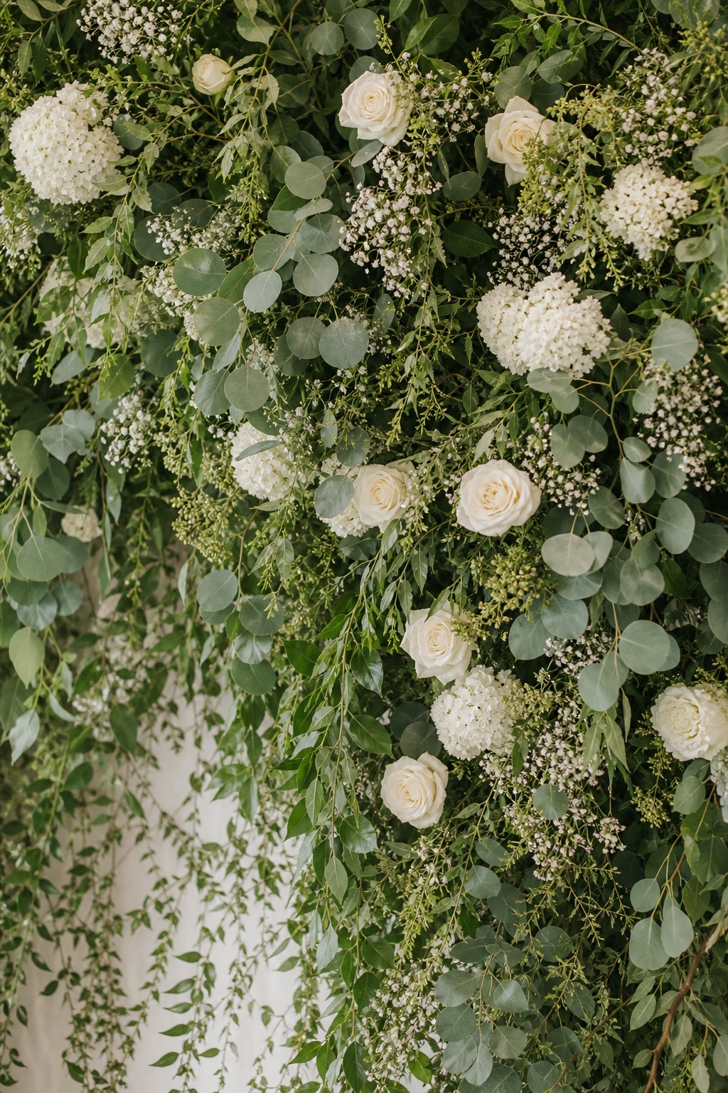 Vertical arrangement of sage eucalyptus leaves, white flowers, and hanging greenery