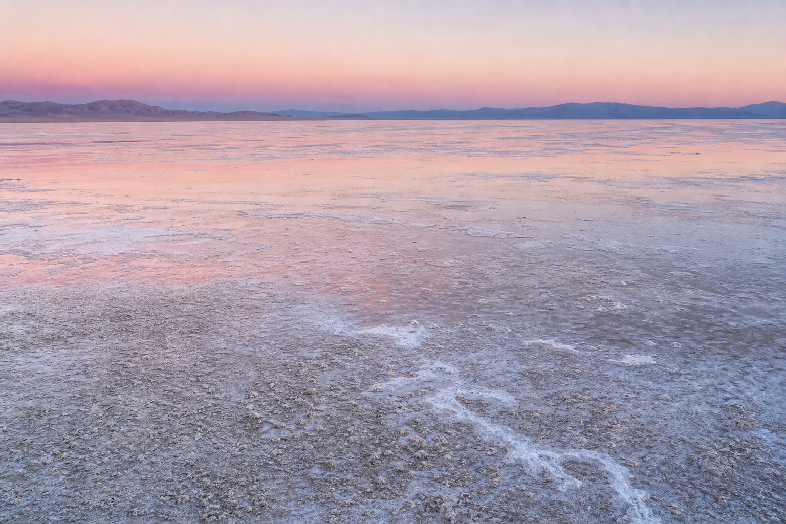 Wide salt flat landscape with a shallow saline sheen under soft dawn light.