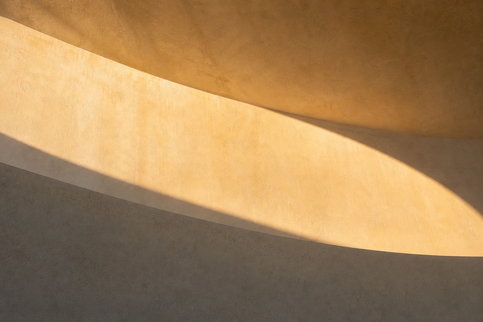 Curved wall casting a soft gold shadow across a muted abstract surface.