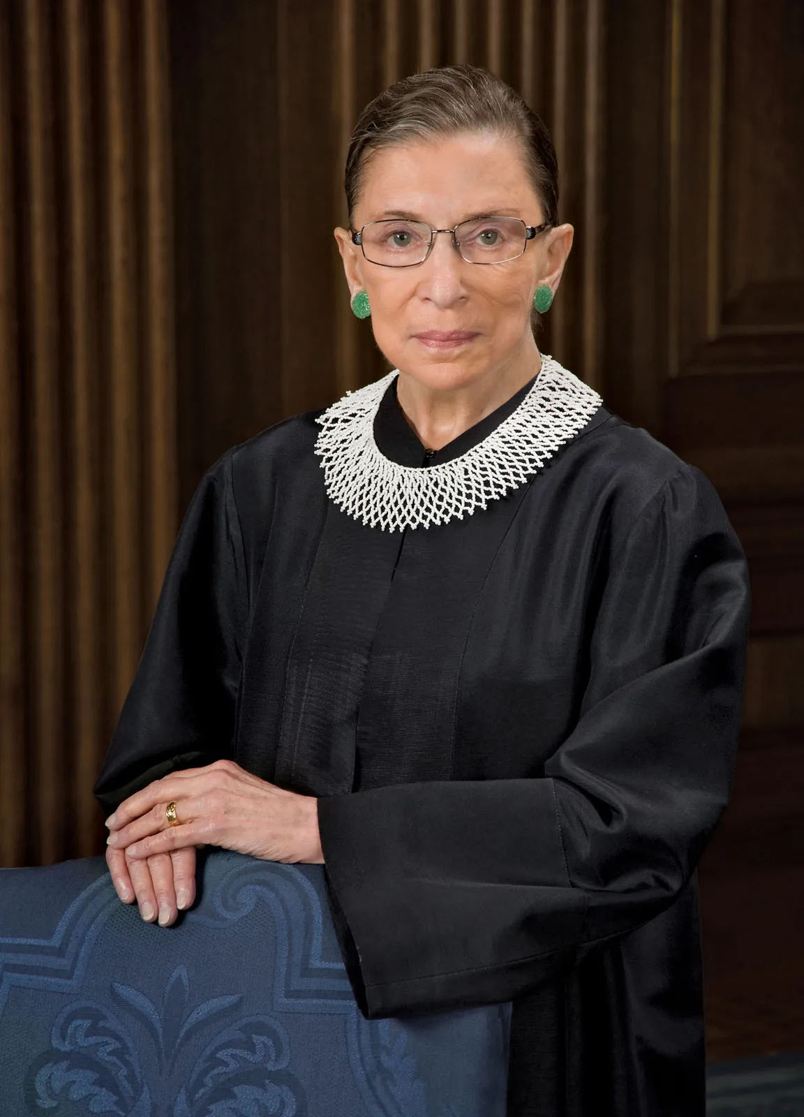 Ruth Bader Ginsburg standing in a black robe beside a patterned blue chair