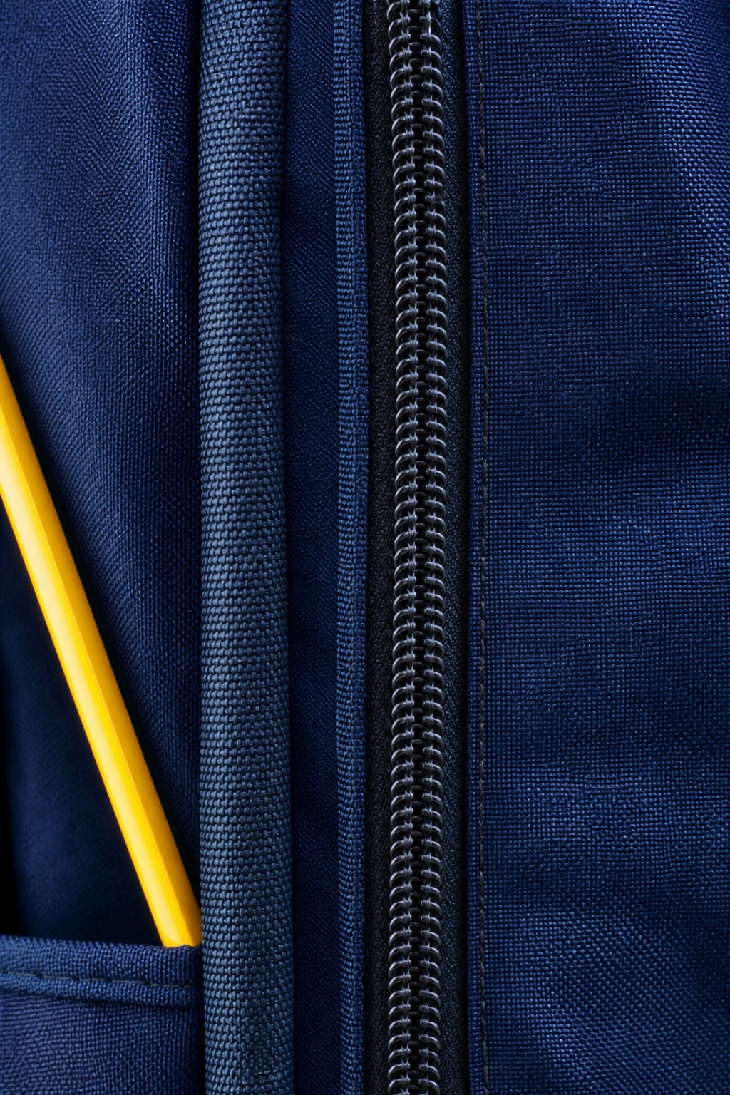 Dark blue backpack fabric with a centered zipper and yellow pencils in the pocket.