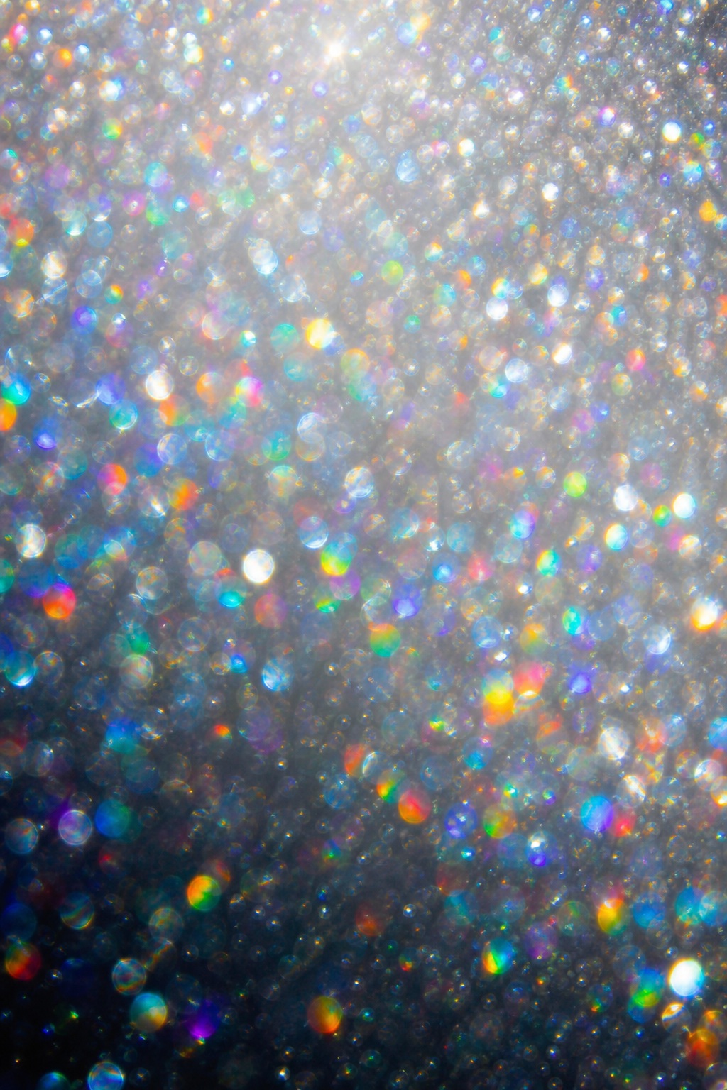 Silver and rainbow prismatic bokeh light flecks on a dark background