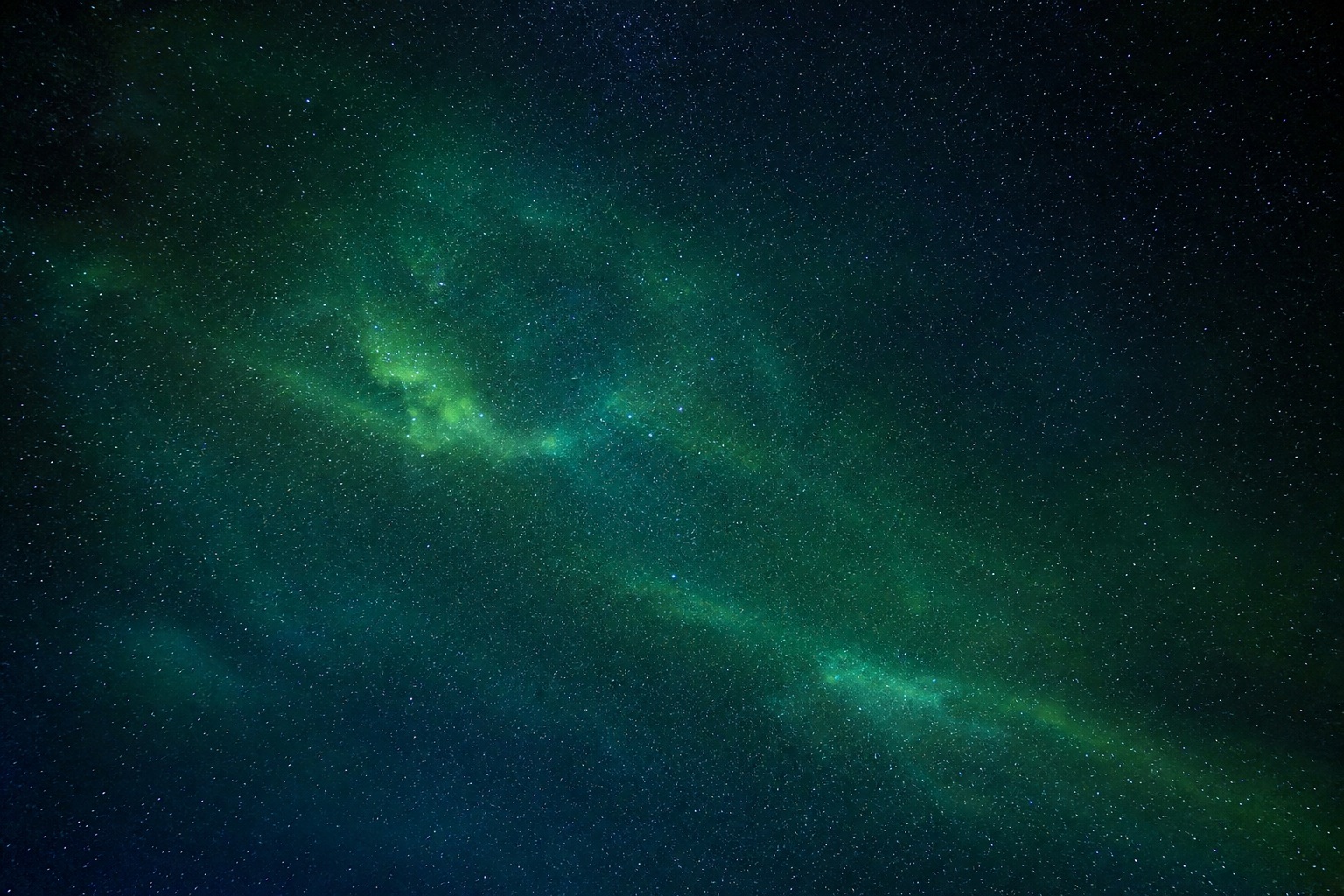 Green aurora glow with a faint star field and distant light cluster in a dark night sky.