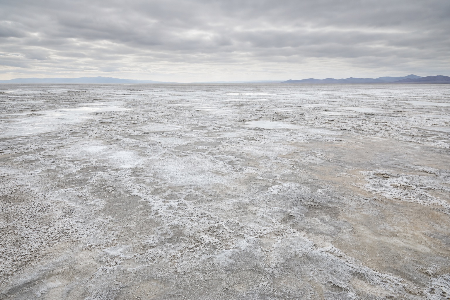 Wide salt flat landscape with weathered mineral crust under a bright overcast sky