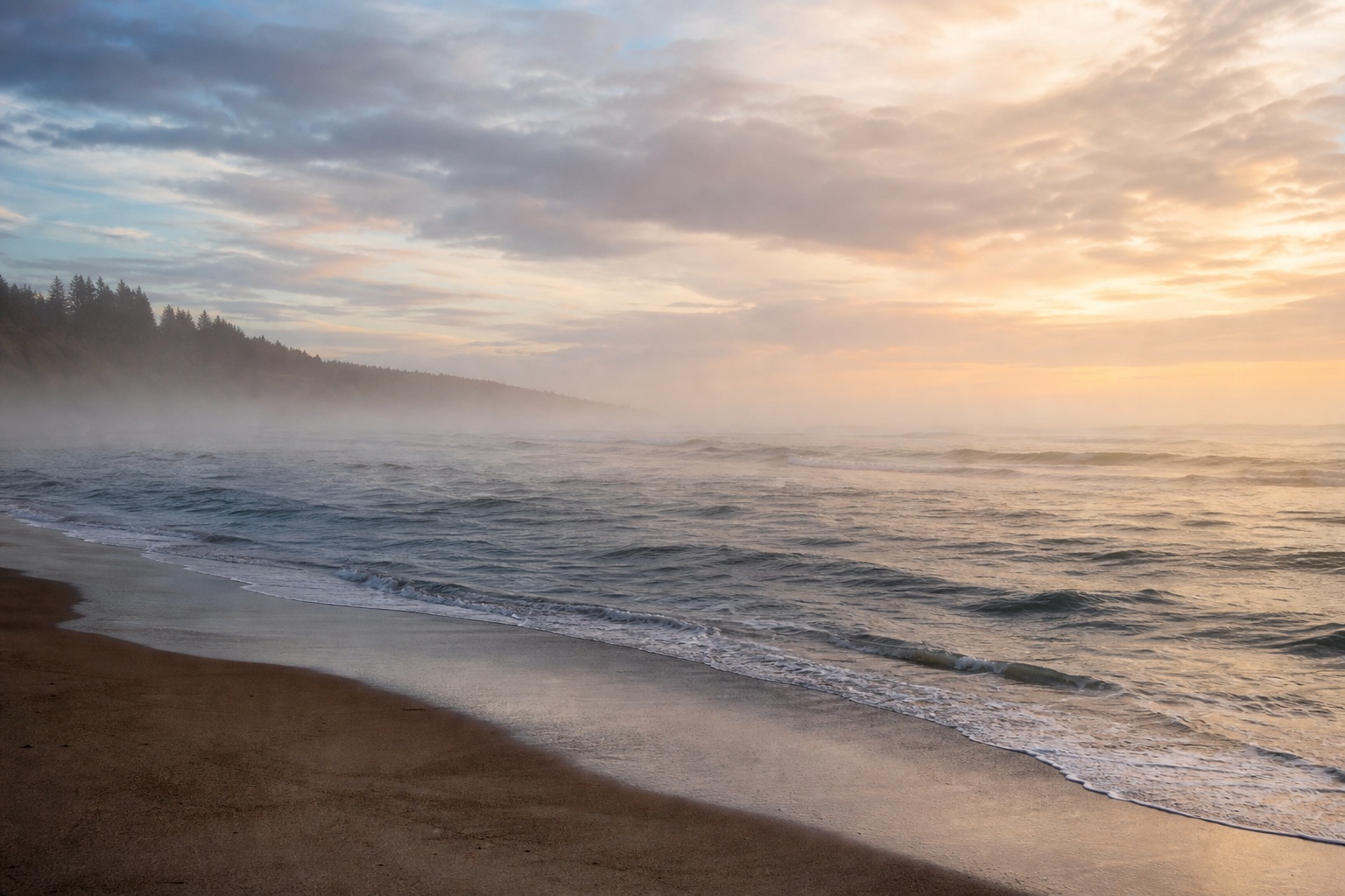 Misty beach shoreline with gentle surf, a distant horizon, and soft sunset light