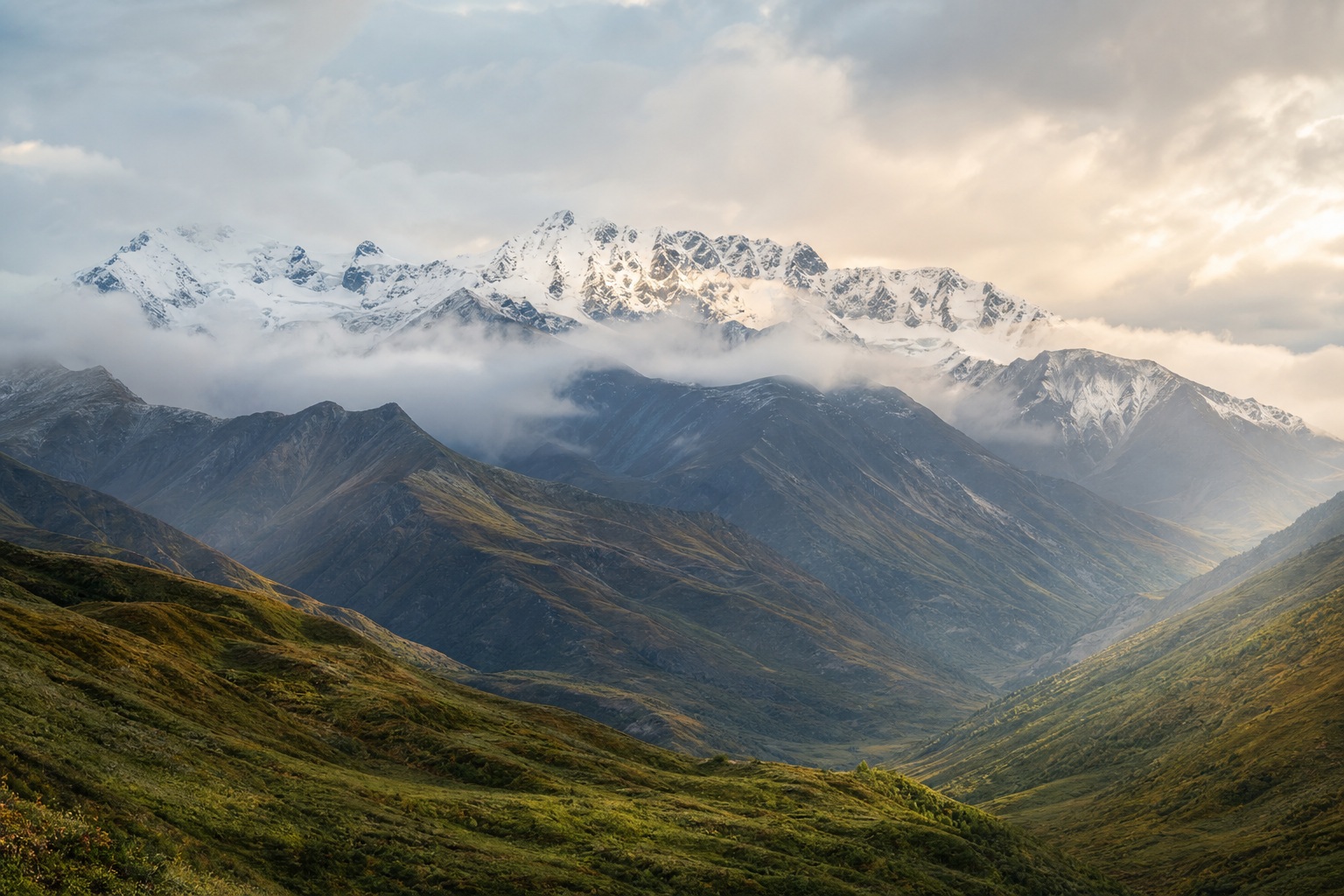 Misty mountain valley with snow-covered peaks and soft light in the distance