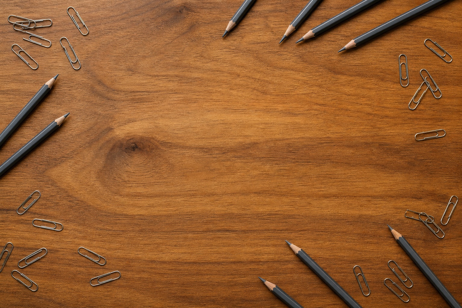 Pencils and paper clips arranged around a wooden desk surface.
