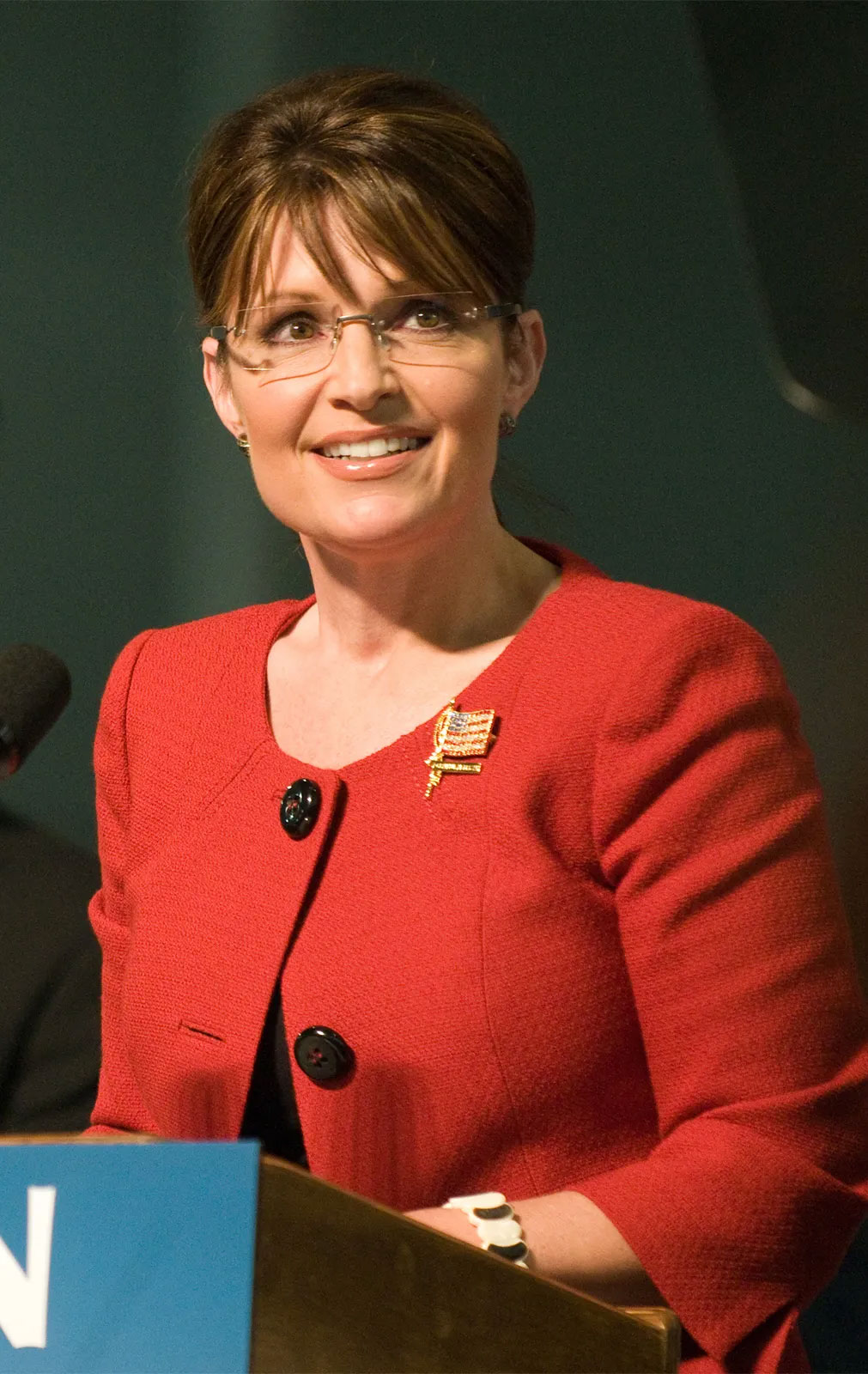 Woman in a red blazer standing at a podium with a microphone