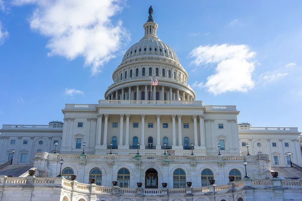 Front view of the United States Capitol Building under a blue sky with clouds.
