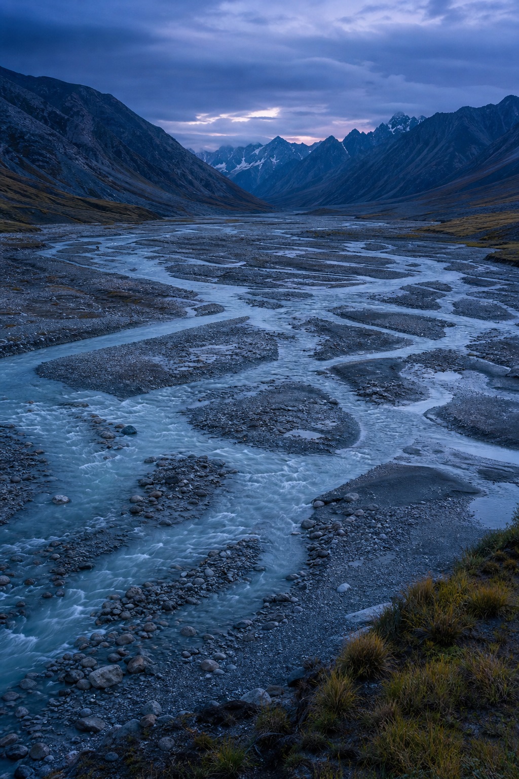 Braided glacial river channels winding through a mountain valley at blue hour