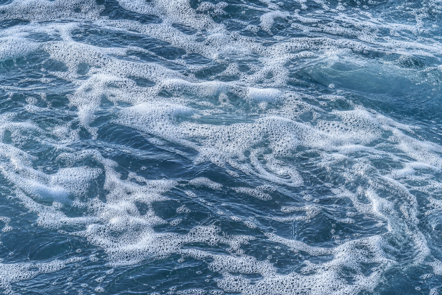 Blue ocean water covered with swirling white sea foam texture