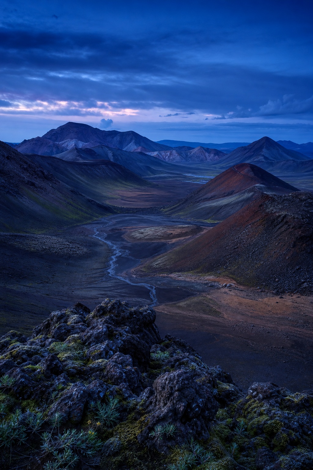 Blue hour view of a volcanic ridge valley with dark basalt slopes and a winding lava plain.