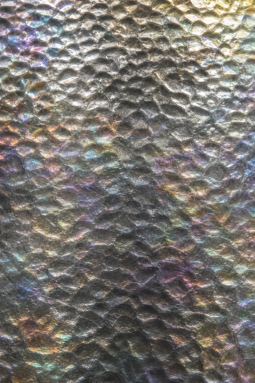 Iridescent graphite foil surface with hammered dimples and rainbow shimmer