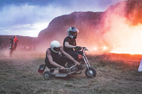 Two men riding a drift trike near a large fire