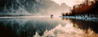 A couple standing on a frozen lake with snow-covered mountains in the background