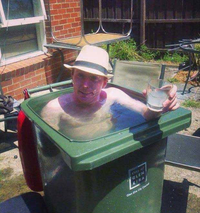 Older man in a hat sitting in a green bin outdoors