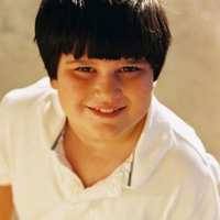 A young boy with dark hair and a white shirt smiling at the camera.