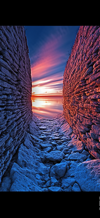 A narrow passage between two rocky walls with a sunset in the background.