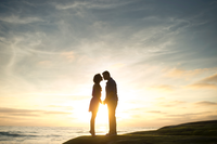 Couple standing on a hill facing each other with a sunset in the background