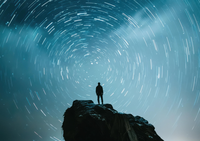 Silhouette of a person on a rocky outcrop under a starry night sky