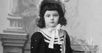 A young child in a formal black dress with a white collar and bow.