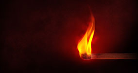 A lit matchstick with a bright orange and yellow flame on a dark surface