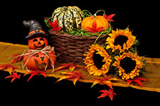 A wicker basket filled with pumpkins and surrounded by sunflowers and fall leaves on a wooden surface.