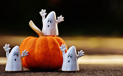 Three white ghost figures around an orange pumpkin