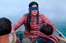 A woman with a blindfold on her eyes is sitting in a boat with two children, surrounded by foggy water.