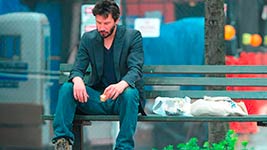 Man sitting on a bench looking down with a bag next to him