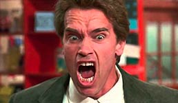 A man in a dark suit and white shirt with an angry expression