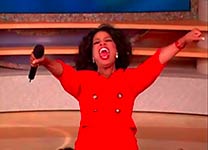 Oprah Winfrey in a red dress holding a microphone and speaking to an audience