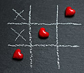 Tic Tac Toe game on a blackboard with red hearts and white chalk marks
