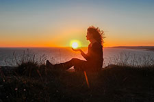Woman meditating at sunset near the ocean
